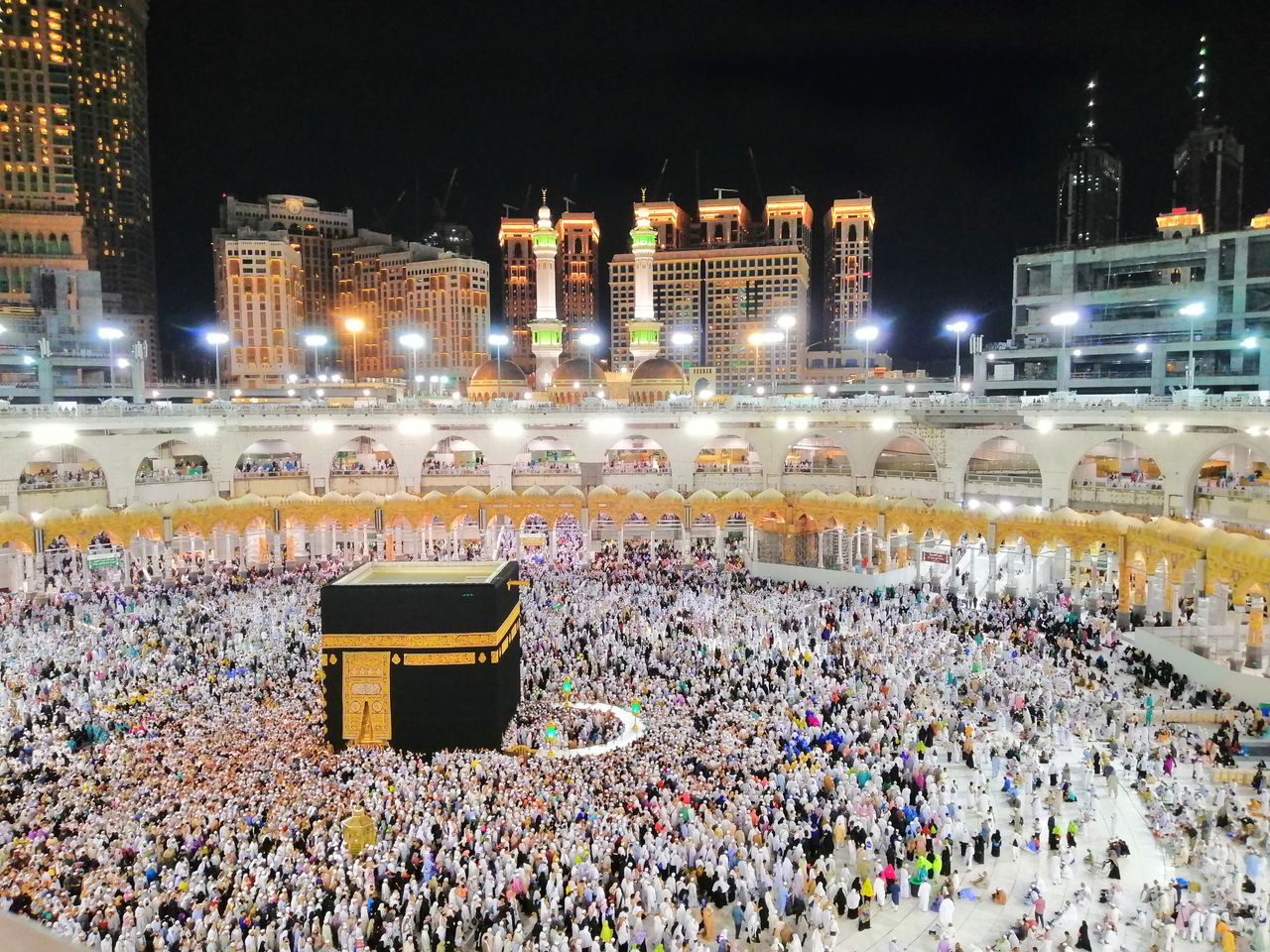 Aerial view of the Kaaba surrounded by pilgrims in Makkah at night, showcasing a religious gathering.